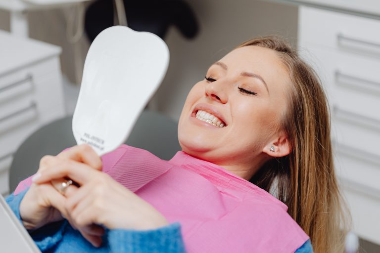 A patient smiling in the dental chair while reviewing her smile in a mirror