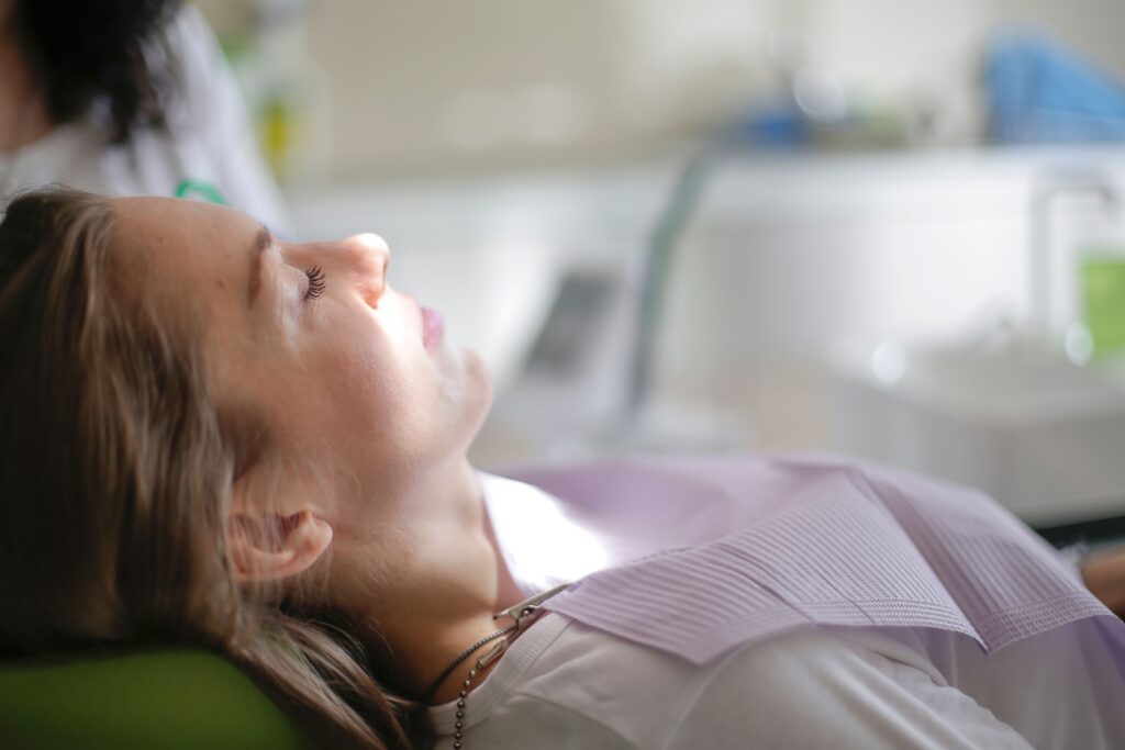 Woman with her eyes closed reclining in a dental chair, wearing a paper bib, in a bright dental office