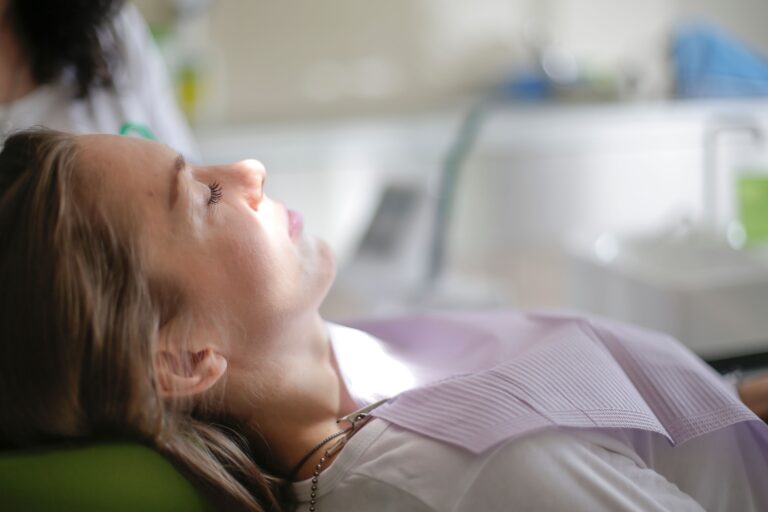 Woman with her eyes closed reclining in a dental chair, wearing a paper bib, in a bright dental office